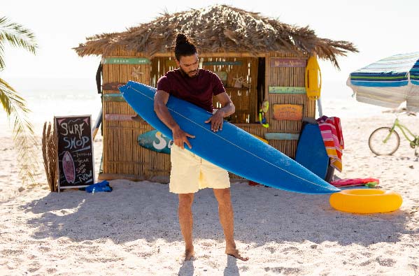 mixed-race-man-holding-surf-board-on-beach